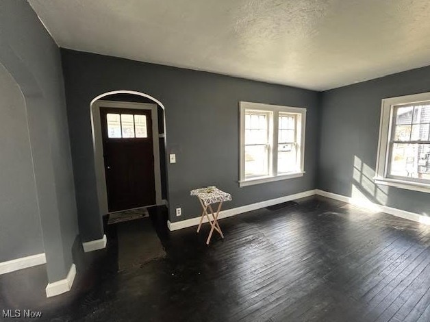 entryway with arched walkways, dark wood-type flooring, and baseboards