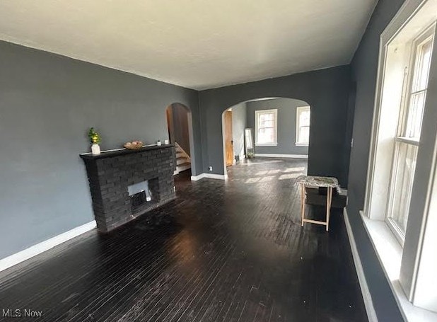 living area with arched walkways, baseboards, and wood finished floors