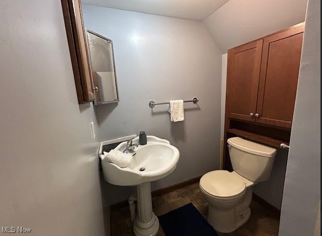 half bath with toilet, baseboards, vaulted ceiling, and a sink