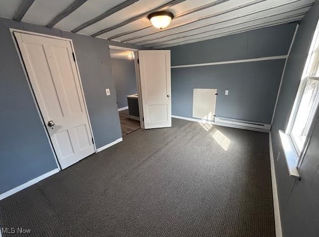 unfurnished bedroom with dark colored carpet, baseboard heating, and baseboards