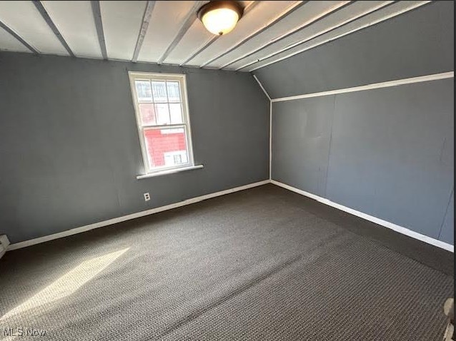 bonus room with vaulted ceiling, dark colored carpet, and baseboards