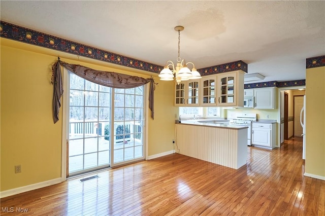 kitchen with a peninsula, white appliances, visible vents, and light wood finished floors