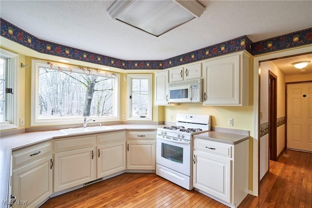 kitchen featuring white appliances, white cabinets, a sink, and light wood finished floors