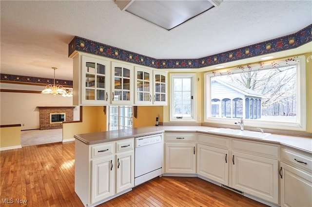 kitchen with dishwasher, a peninsula, light wood-type flooring, white cabinetry, and a sink