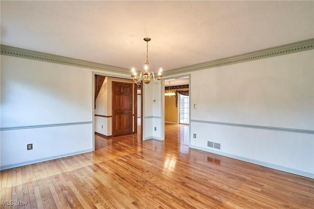 spare room with a chandelier, visible vents, crown molding, and hardwood / wood-style floors