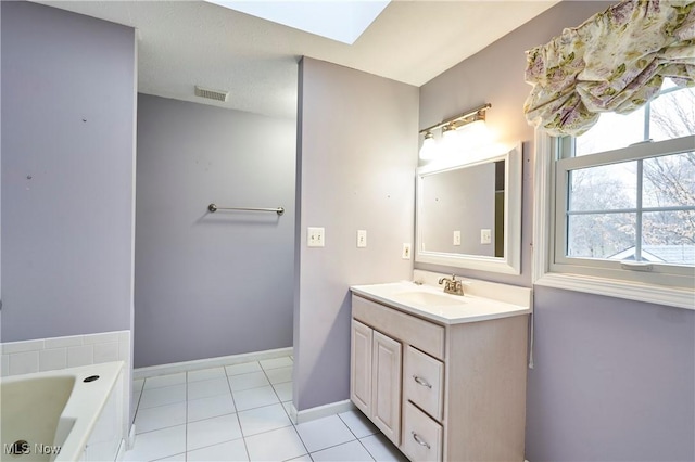 bathroom featuring a skylight, vanity, visible vents, baseboards, and a bath