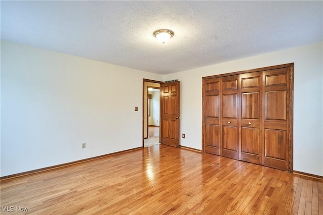 unfurnished bedroom featuring light wood-style floors, a closet, baseboards, and a textured ceiling