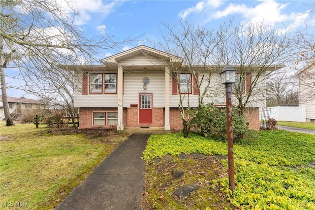 bi-level home featuring fence, a front lawn, and brick siding