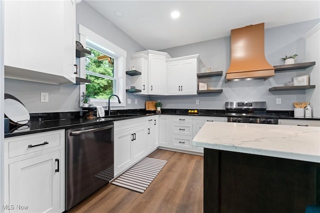 kitchen with open shelves, appliances with stainless steel finishes, a sink, wood finished floors, and premium range hood