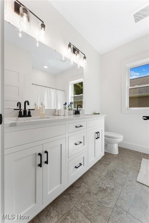 bathroom with toilet, double vanity, a wealth of natural light, and visible vents