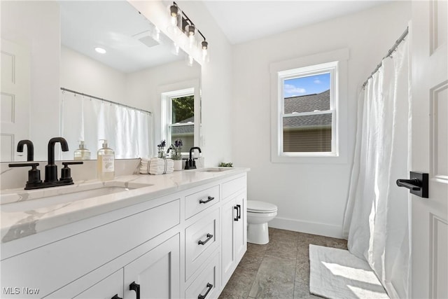 full bathroom featuring toilet, double vanity, baseboards, and a sink