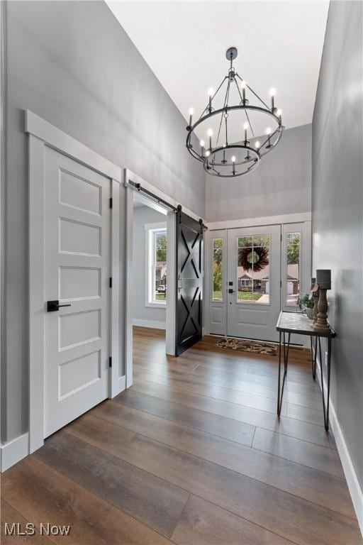 entryway featuring a barn door, baseboards, dark wood-style floors, an inviting chandelier, and a high ceiling