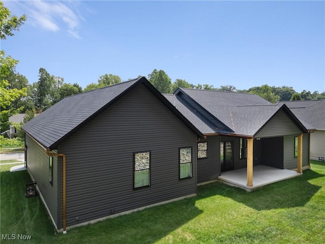 rear view of house with a yard, a patio, and a shingled roof