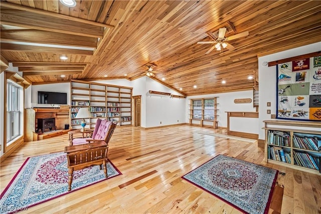 living area featuring a fireplace with raised hearth, wooden ceiling, ceiling fan, hardwood / wood-style floors, and vaulted ceiling with beams