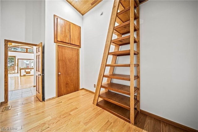 staircase featuring high vaulted ceiling, visible vents, baseboards, and wood finished floors