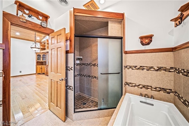 bathroom featuring a garden tub, a shower stall, visible vents, and tile walls