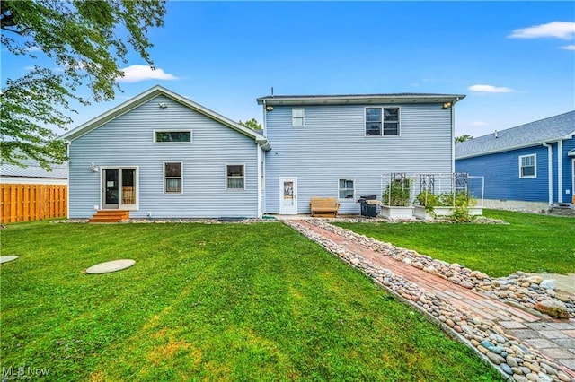 rear view of property featuring entry steps, a yard, and fence