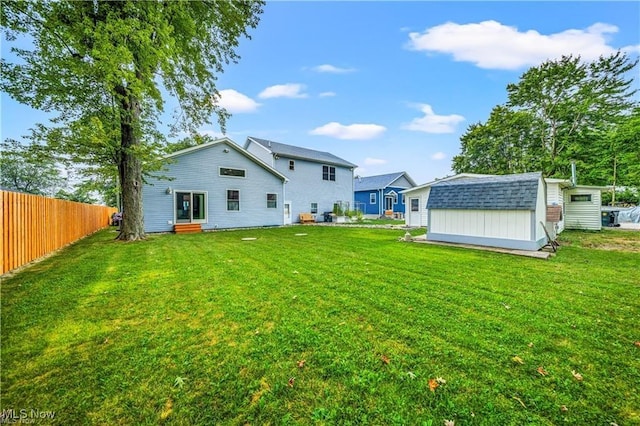 back of house with a storage shed, a yard, an outbuilding, and fence