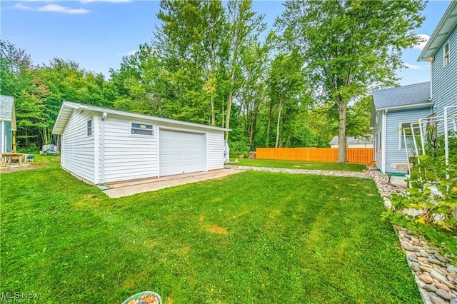 view of yard featuring a garage, fence, driveway, and an outdoor structure