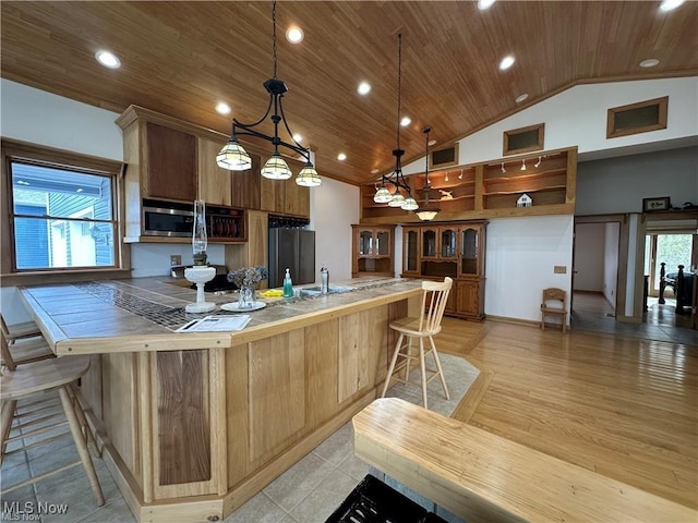 kitchen with tile countertops, stainless steel appliances, a sink, wooden ceiling, and a kitchen bar