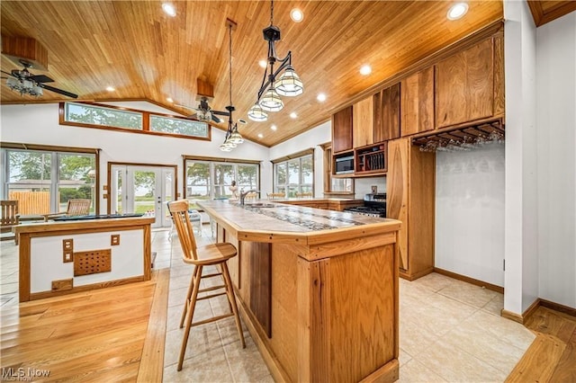 kitchen with light countertops, appliances with stainless steel finishes, brown cabinetry, wood ceiling, and a kitchen island with sink