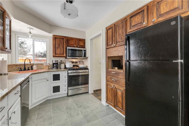 kitchen with stainless steel appliances, a sink, white cabinetry, light stone countertops, and glass insert cabinets