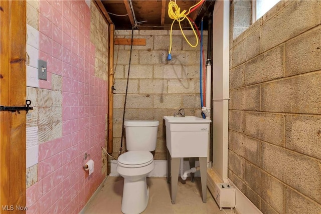 half bathroom featuring concrete flooring, concrete block wall, and toilet