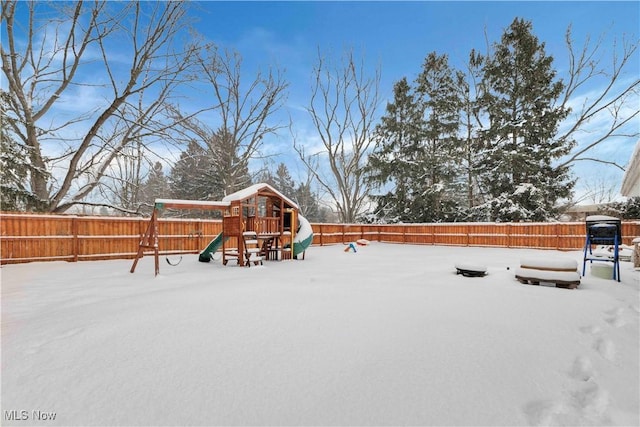 yard layered in snow featuring a playground and a fenced backyard