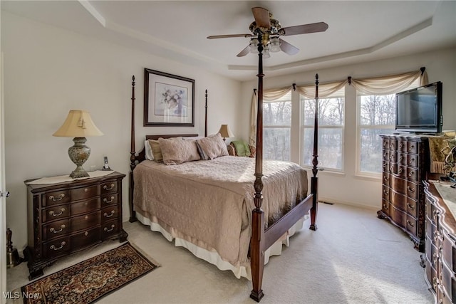 bedroom featuring a raised ceiling, a ceiling fan, and light colored carpet