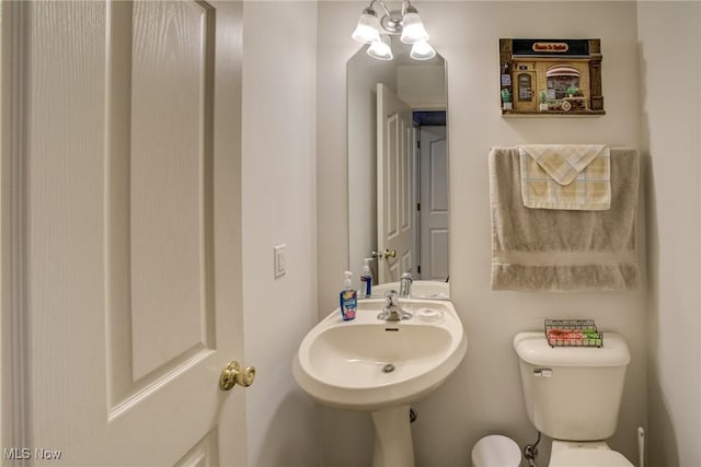 half bath with toilet, an inviting chandelier, and a sink