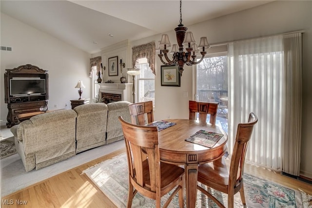 dining area featuring lofted ceiling, a fireplace, light wood finished floors, and an inviting chandelier