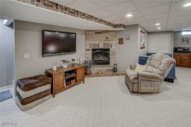 living room featuring light colored carpet, a drop ceiling, a stone fireplace, and recessed lighting