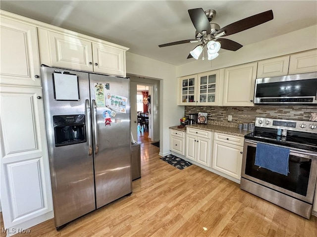 kitchen with stainless steel appliances, white cabinets, light wood-style floors, and backsplash