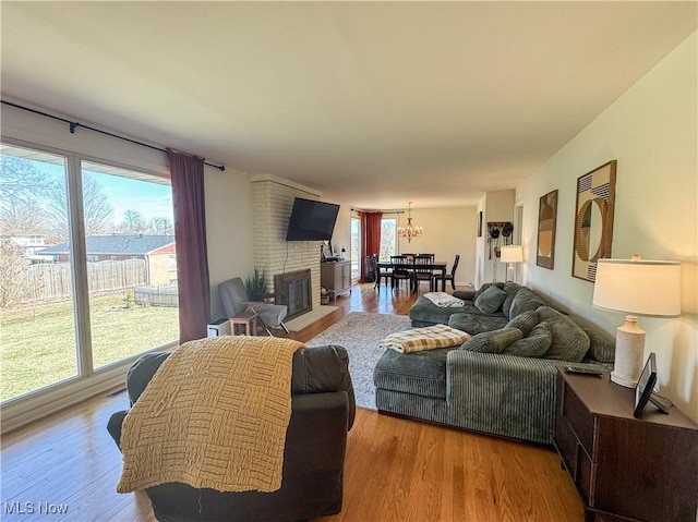 living area with a brick fireplace, a chandelier, and wood finished floors