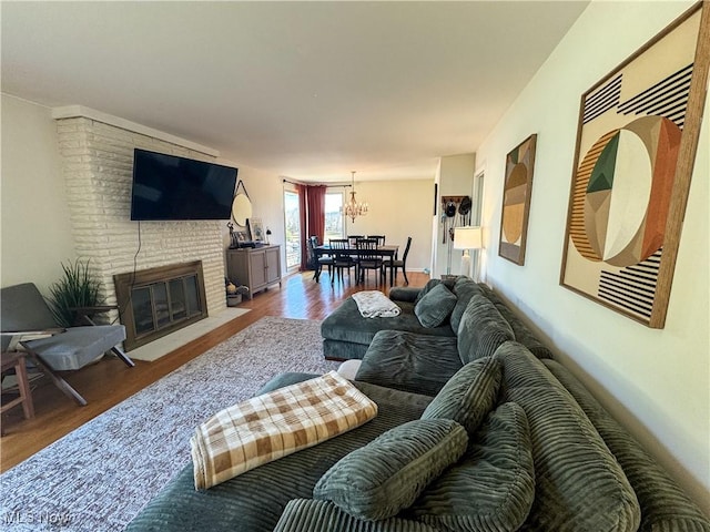 living area with a brick fireplace, wood finished floors, and an inviting chandelier