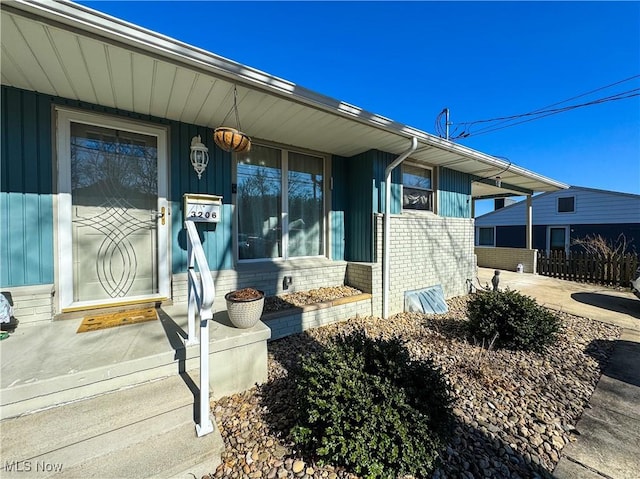 doorway to property featuring an attached carport, concrete driveway, and brick siding