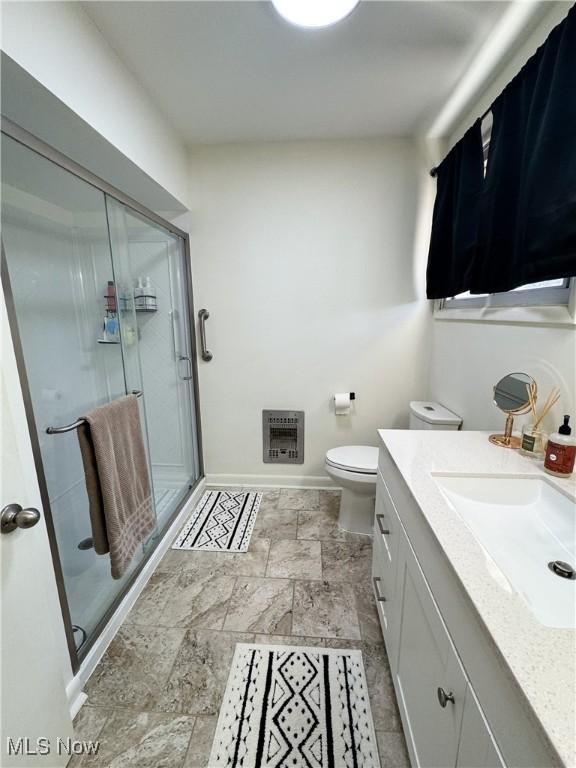 bathroom with baseboards, stone finish floor, heating unit, vanity, and a shower stall