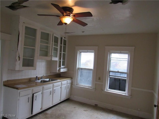 kitchen with baseboards, white cabinets, decorative backsplash, glass insert cabinets, and a sink