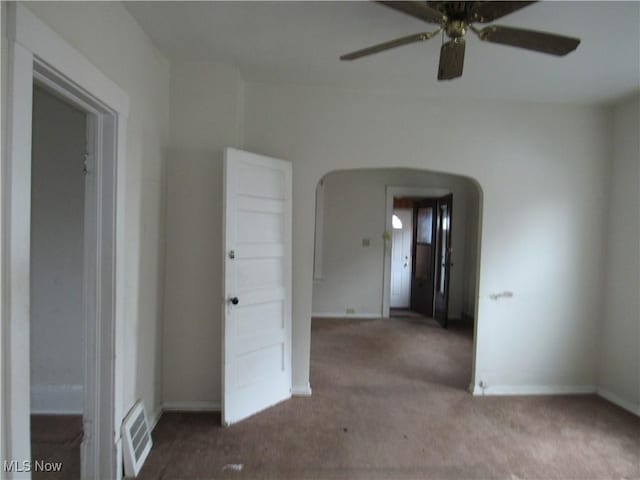 carpeted spare room featuring arched walkways, ceiling fan, visible vents, and baseboards