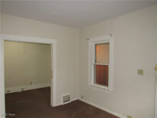 unfurnished room featuring baseboards, visible vents, and dark colored carpet