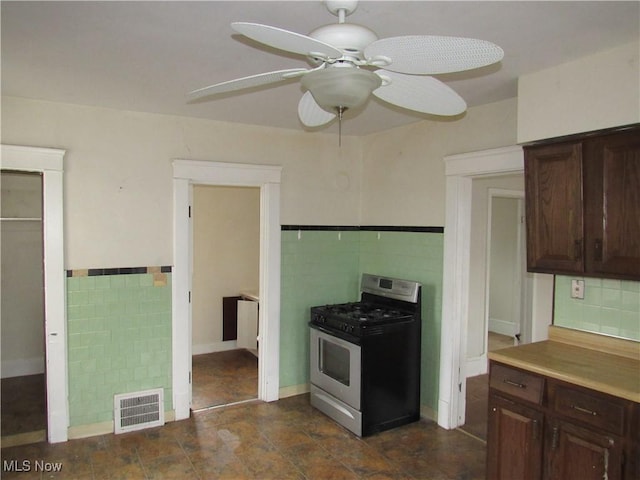 kitchen featuring stainless steel gas range, visible vents, dark brown cabinets, and tile walls