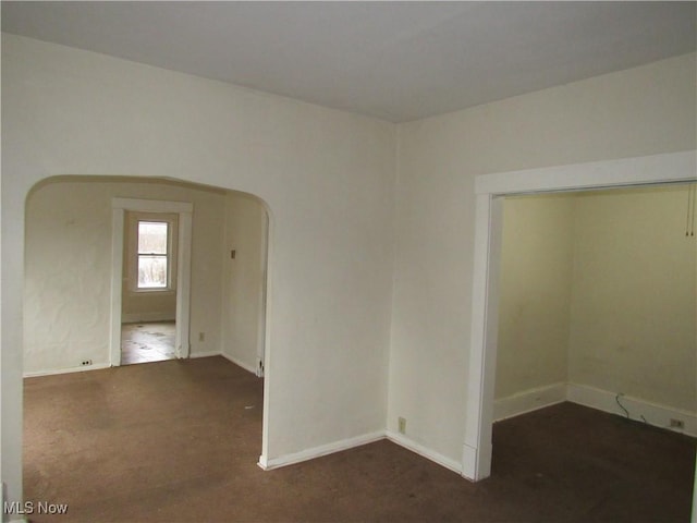 carpeted spare room with arched walkways and baseboards