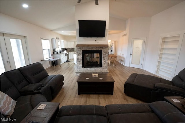 living area with light wood-type flooring, high vaulted ceiling, a fireplace, and visible vents