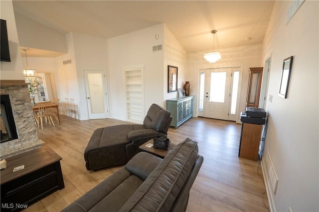 living room featuring high vaulted ceiling, a stone fireplace, wood finished floors, and visible vents