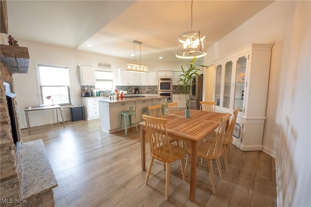 dining area featuring a stone fireplace, light wood-type flooring, recessed lighting, and a notable chandelier