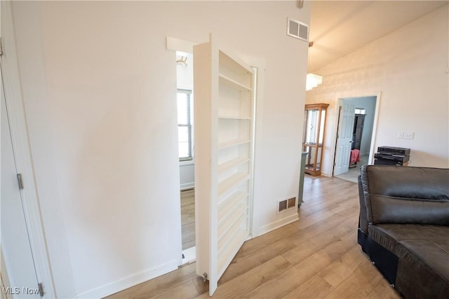 hall with light wood-style flooring, visible vents, vaulted ceiling, and baseboards