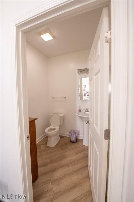 half bathroom with baseboards, toilet, and wood finished floors