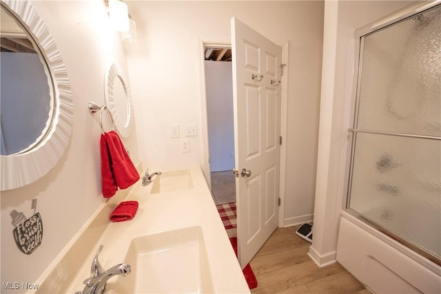 bathroom featuring double vanity, enclosed tub / shower combo, a sink, and wood finished floors