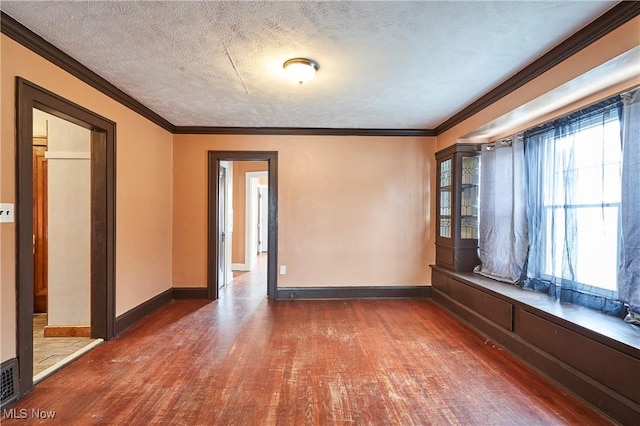 empty room with wood-type flooring, a textured ceiling, baseboards, and crown molding