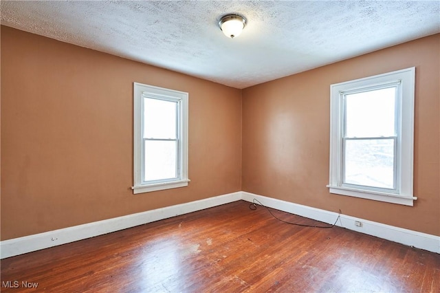 spare room with a textured ceiling, wood finished floors, and baseboards